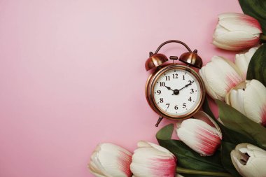 Pembe arka planda klasik çalar saat ve lale çiçeği buketi.