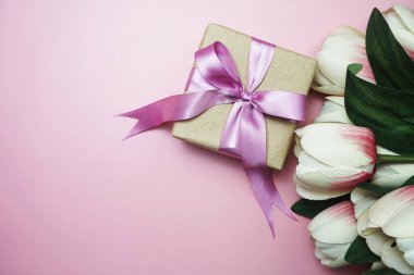Pembe kurdeleli hediye kutuları ve pembe arka planda lale çiçeği buketi.