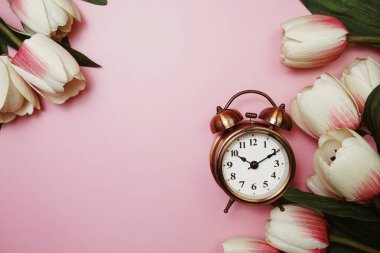 Pembe arka planda klasik çalar saat ve lale çiçeği buketi.