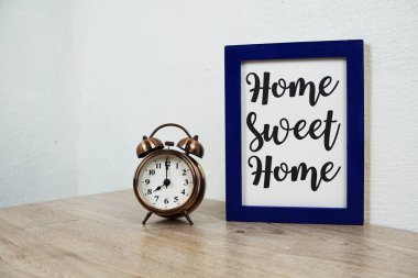 Home Sweet Home tipografisi ahşap masa ve beyaz duvar arkaplanı üzerindeki alarm saati