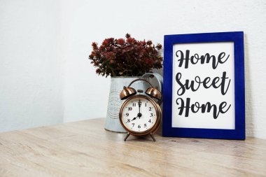 Home Sweet Home tipografisi ahşap masa ve beyaz duvar arkaplanı üzerindeki alarm saati