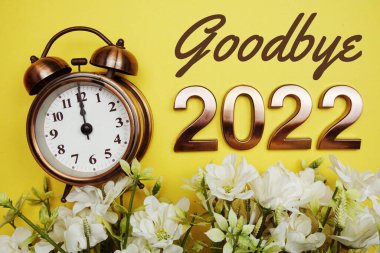 Güle güle 2022 yazıları çalar saat ve sarı arkaplanda çiçek süslemesi