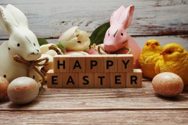 Çiçekli, tavşanlı ve tahta arka planda paskalya yumurtası süslemeli mutlu Paskalyalar.