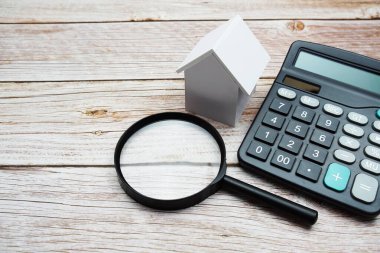 Ahşap zemin üzerinde büyüteç ve hesap makinesi olan Beyaz Model Evi, emlak konsepti