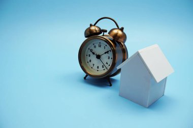 Alarm saati ve ev modeli mavi arkaplanda boşluk kopyası