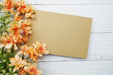 Tahta zemin üzerinde turuncu papatya çiçeği bezi olan boş bir kağıt kart.