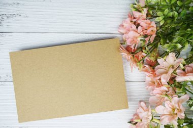 Tahta zemin üzerinde pembe papatya çiçeği bezi olan boş bir kağıt kart.