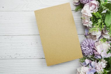 Çiçek buketi ve çalar saati olan boş kağıt kart tahta arka planda yatıyordu.