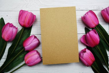 Boş kağıt kart, pembe lale çiçeği ve çalar saati olan tahta arka planda yatıyordu.