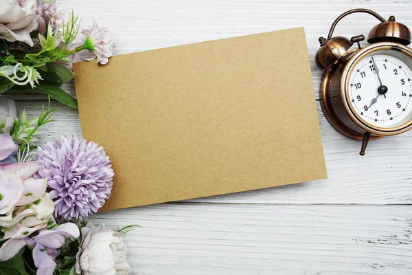 Boş kağıt kart çiçek ve çalar saat düz ahşap zemin üzerinde yatıyordu
