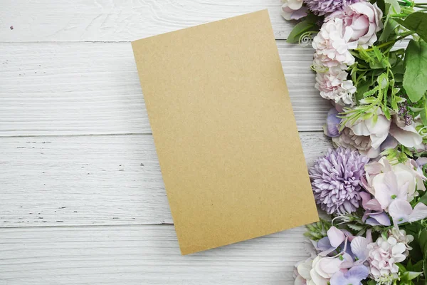 Çiçek buketi ve çalar saati olan boş kağıt kart tahta arka planda yatıyordu.