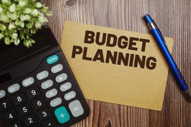 Tahta arkaplanda hesap makinesi olan kağıt kart üzerindeki bütçe planlama tipografisi metni