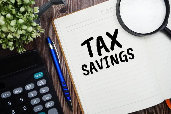 Tahta arkaplanda hesap makinesi olan kağıt kart üzerinde Vergi Tasarruf tipografisi metni