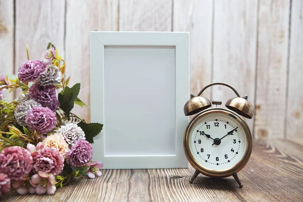 Alarm saati ve boş çerçeve dekorasyonu. Ahşap arka planda çiçek buketi var.