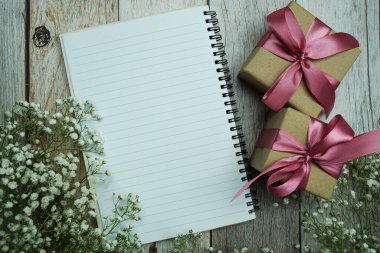 Not defteri ve hediye kutusunda pembe kurdele ve ahşap arka planda çiçek süslemesi.