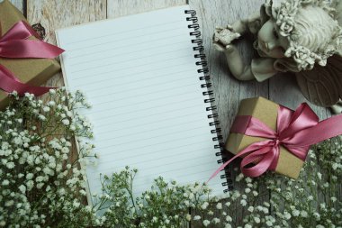 Not defteri ve hediye kutusunda pembe kurdele ve ahşap arka planda çiçek süslemesi.
