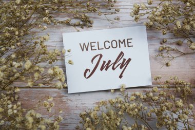 Tahta arka planda çiçek süslemesi olan kağıt kart üzerine Temmuz ayına hoşgeldiniz metni