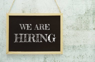 We are Hiring typography text on wooden blackboard hanging on concrete background