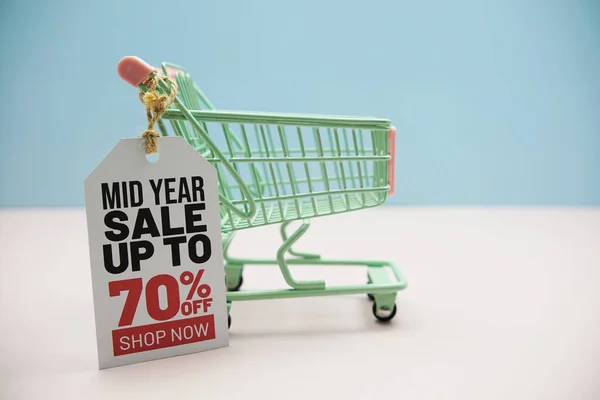 Mid Year Sale up to 70% text message on price tax with shoppint trolley cart on blue andp pink background