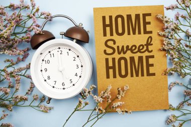 Home sweet home written on paper card with flower and alarm clock on blue background