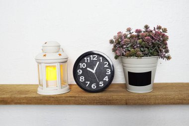 White lantern, black alarm clock and artificil plant on wooden shelves