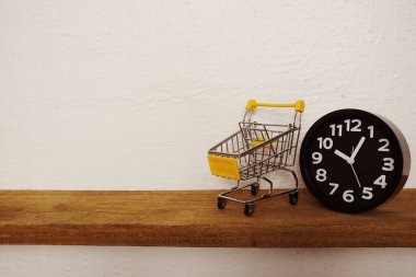 Mini trolley shopping cart with black alarm clock on wooden shelves