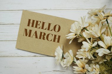 Hello March written on paper card and flower bouquet on wooden background