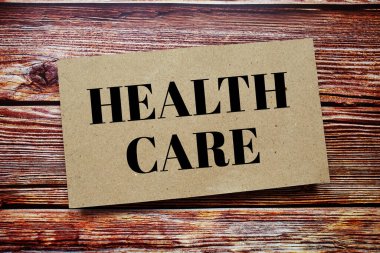 Health Care written on paper card top view of wooden background
