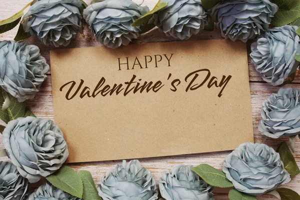 Happy Valentine\'s Day written on paper card and rose flower bouquet on wooden background