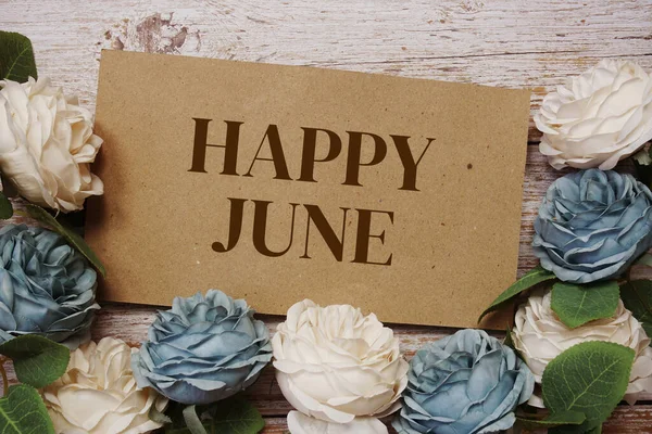 Happy June written on paper card and rose flower bouquet on wooden background