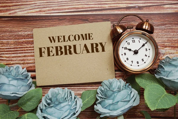 Welcome February written on paper card and rose flower bouquet on wooden background