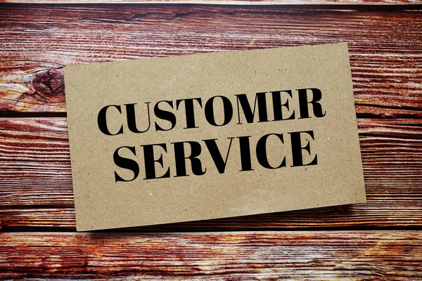 Customer Service written on paper card top view of wooden background