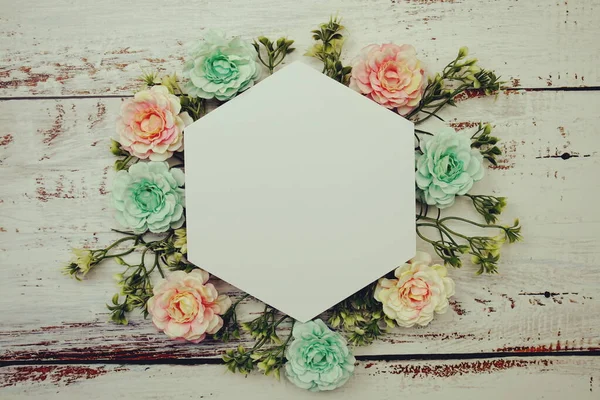 Frame of flowers with paper card for text on wooden background