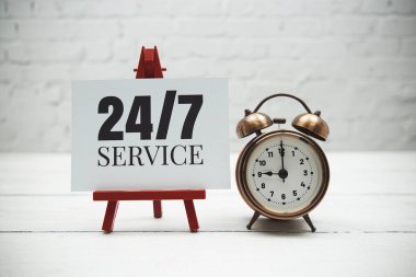 24 Hour  text and alarm clock on white brick wall and wooden background
