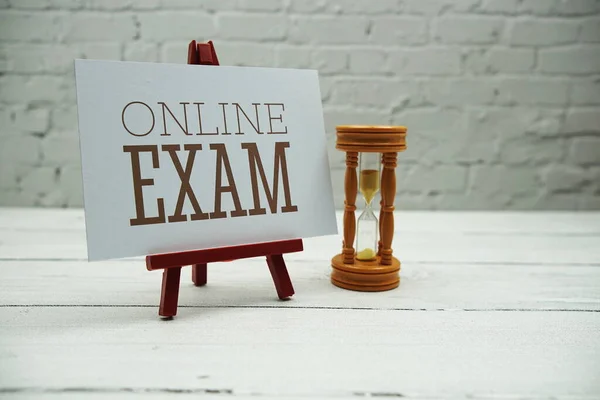 Online Exam text and sandglass on white brick wall and wooden background