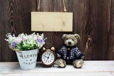 Tahta arka planda oyuncak ayı ve çalar saatle asılı boş tahta tabela