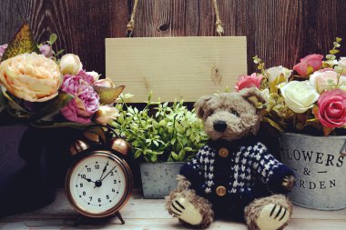 Tahta arka planda oyuncak ayı ve çalar saatle asılı boş tahta tabela