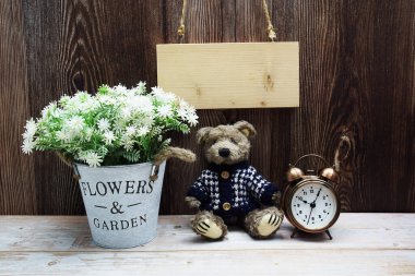 Tahta arka planda oyuncak ayı ve çalar saatle asılı boş tahta tabela