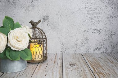 Beton ve ahşap zemin üzerinde yapay çiçekli LED mum ışığı olan kuş kafesi