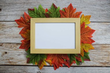 Ahşap zemin üzerinde akçaağaç yaprakları olan fotoğraf çerçevesini boşalt