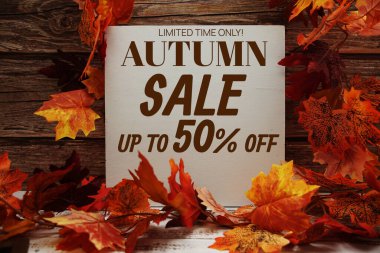 Sonbahar İndirimi metin mesajı. Ahşap zemin üzerinde sonbahar akçaağaç yaprakları ve balkabakları var.