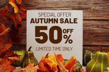 Sonbahar İndirimi metin mesajı. Ahşap zemin üzerinde sonbahar akçaağaç yaprakları ve balkabakları var.