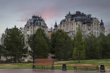 Kozalaklı ağaçlar sokağında banklar ve güzel binalar Ön planda