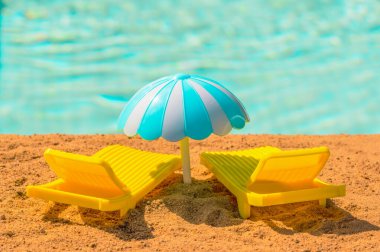 Sıcak bir günde plajda iki sarı oyuncak güneş şezlongu ve bir şemsiye. Su havuzu, deniz ya da okyanus kenarında rahatlayın. Stok fotoğrafı