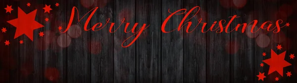 メリークリスマスお祝いの背景バナーパノラマグリーティングカード 素朴な黒い木の板の上に赤い星 手のレタリングとボケライト 木の壁のテクスチャ — ストック写真