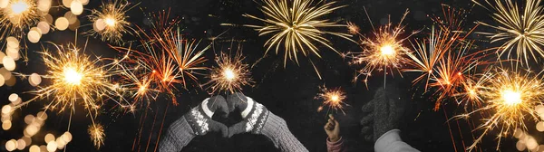 Happy New Year / Silvester / Party background banner panorama greeting card - Young happy people holding sparkling sparklers in her hands at dark night, with golden bokeh lights and firework