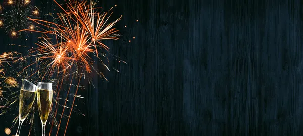 Mutlu yeni yıl pankartı uzun havai fişekler, altın havai fişekler, şampanya kadehleri ve kırsal mavi ahşap dokuda bokeh ışıkları.