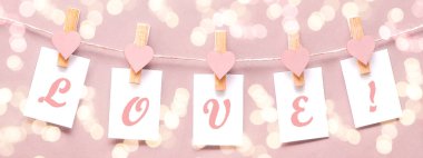 Aşkım - Ahşap kalpli ve kağıt notlu elbise askıları yumuşak pastel renkte izole edilmiş ipe asılır. Pembe dokuda bokeh ışıkları arka planda panorama uzunluğunda, metin için yeri olan panorama