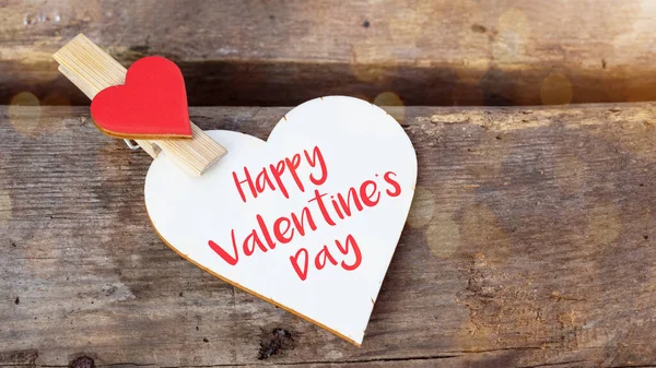 Sevgililer Günü tebrik kartı şablonu ahşaptan yapılmış kalp, kırsal ahşap masa dokusunda kırmızı kalpli ahşap mandallar.