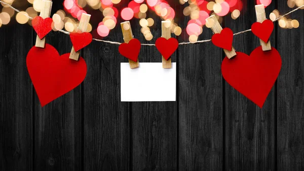 情人节快乐的背景 红色的心和白色的纸条挂在木制的衣服钉上 木制的心和孤立在黑色的木制墙壁上的绳子上的爆竹灯 上面有文字的空间 — 图库照片